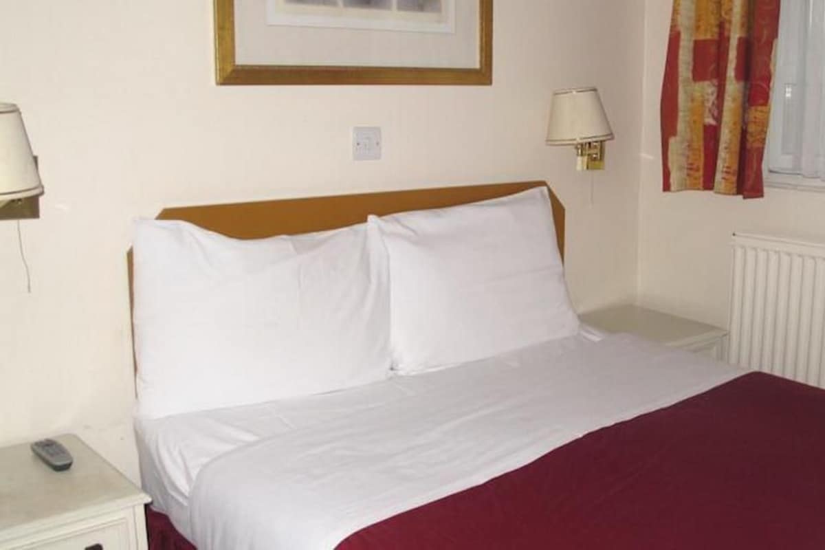 A hotel room with a bed, a nightstand, a lamp, and a window with curtains.