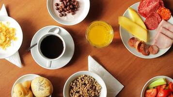 Een ontbijttafel met diverse soorten eten, zoals cornflakes, worst, kaas en fruit.