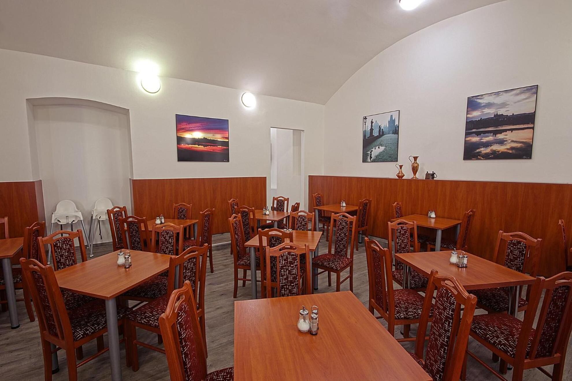 Un restaurant amb diverses taules i caires, que destaca per un quadre del capvespre i un altre del paisatge urbà a les parets.