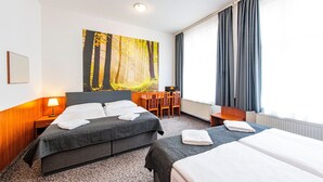 Habitación de hotel con dos camas, un cuadro grande con tema de bosque en la pared, una mesa de comedor con sillas y una ventana con cortinas.