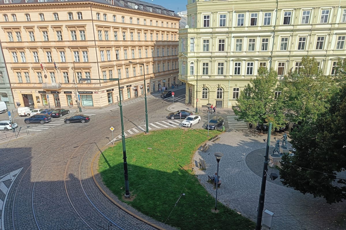 A city street with tram tracks, buildings, and a grassy area.