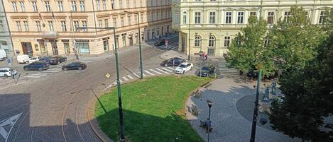 A city street with tram tracks, buildings, and a grassy area.