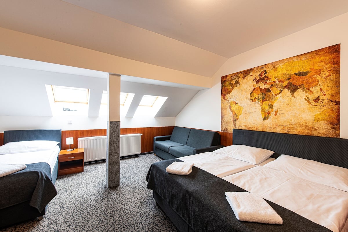 A hotel room with two beds, a large world map on the wall, skylights, and a patterned carpet.