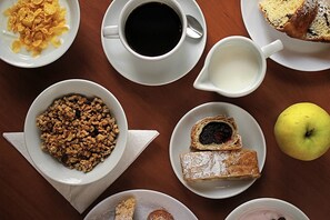 A breakfast setting with cereal, coffee, milk, pastries, and an apple on a wooden table. - Hotel Zlatá Váha (Prague)