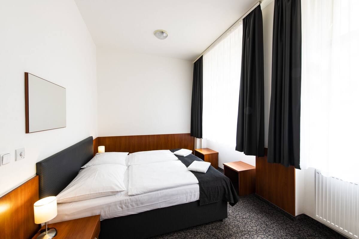 A hotel room with a bed, bedside tables, a lamp, a mirror, and a window with curtains.