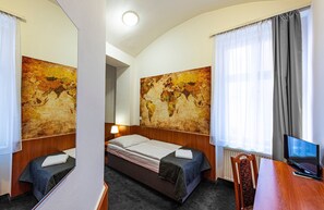 A hotel room with a single bed, a desk with a computer, and two large world maps on the walls. - Hotel Zlatá Váha (Prague)