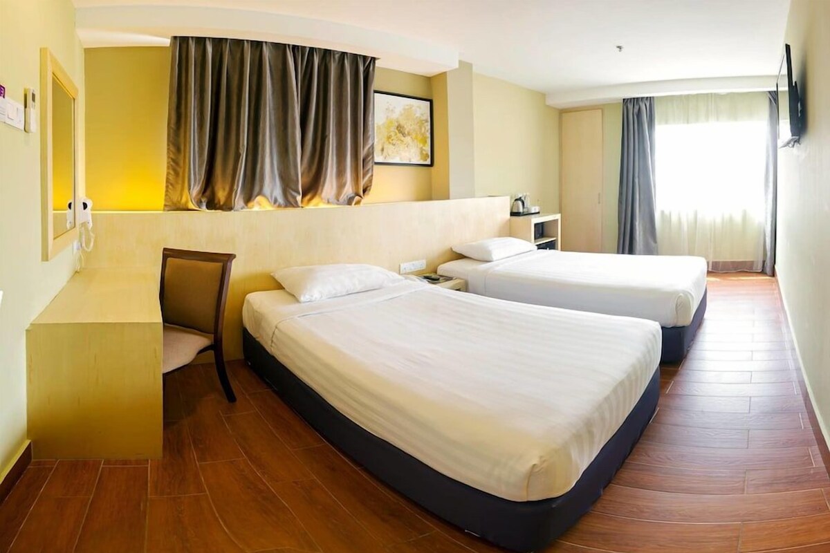A hotel room with two single beds, a desk, a chair, a TV, and a window with curtains.