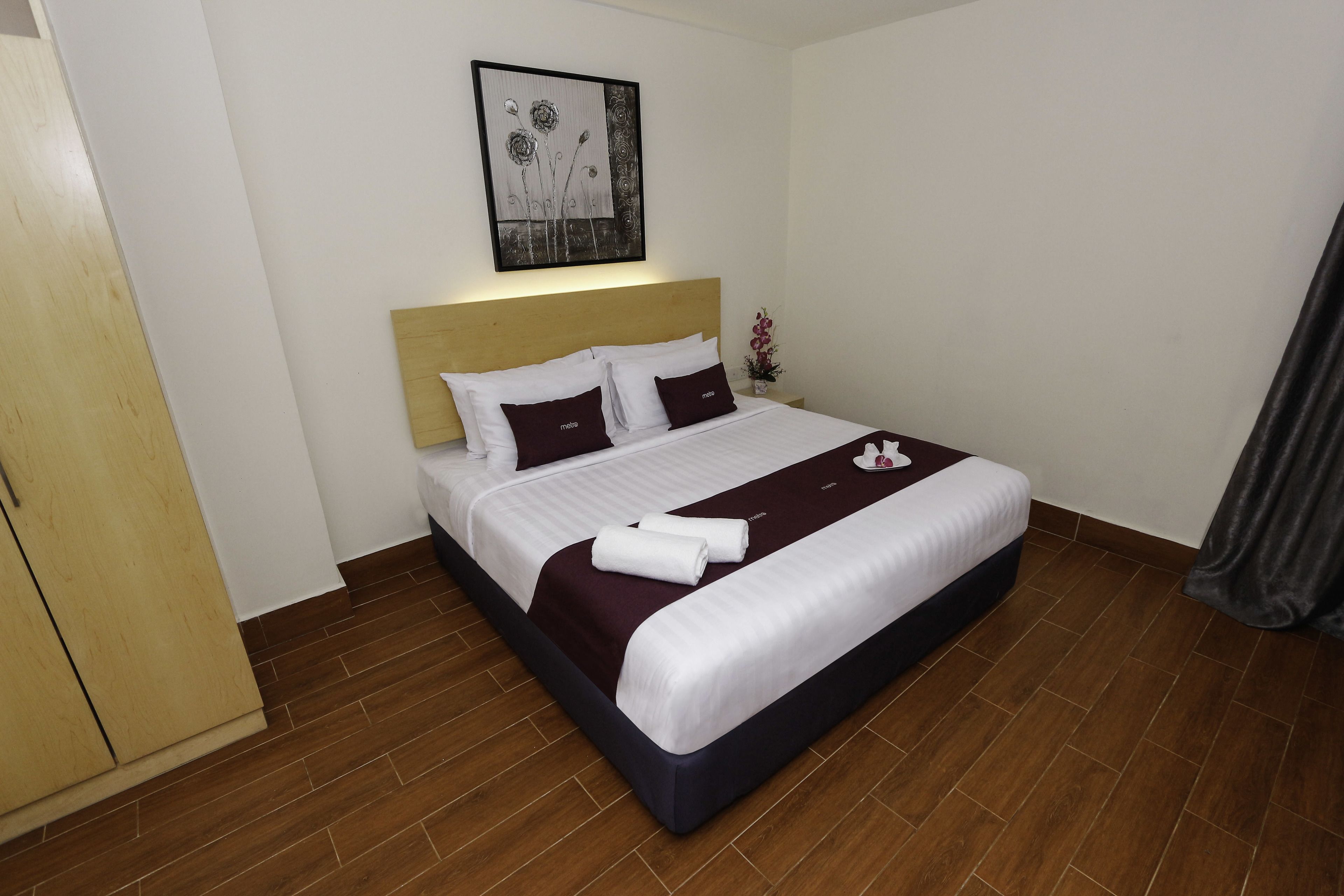 A hotel room with a large bed, a wooden headboard, a wall-mounted artwork, and a small potted plant.