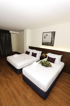 Habitación de hotel con dos camas, piso de madera, un cuadro en la pared y una mesita de noche con frutero.