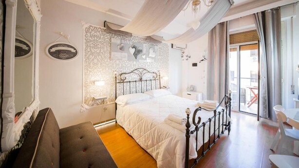 A bedroom with a bed, a bedside table, a chair, and a window with curtains. - Casale D'Or (Palermo)