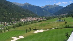 A golf course with sand bunkers, a town in the valley, and mountains in the background. - Garní al Nardis (Carisolo)