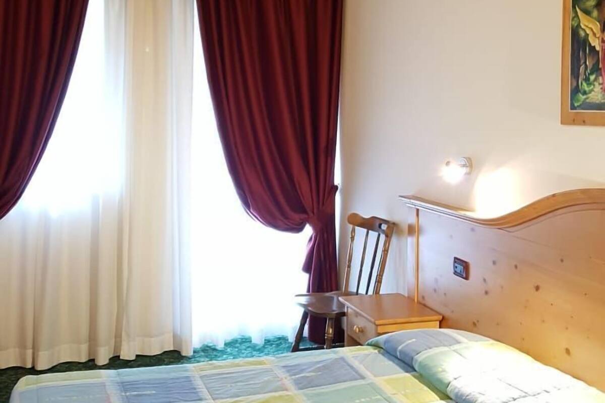 A bedroom with a wooden ceiling, a bed with a colorful quilt, a chair, and a painting on the wall.
