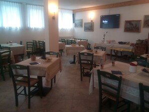A dining area with multiple tables and chairs, a television mounted on the wall, and framed pictures on the walls.