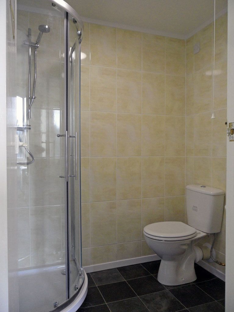 A bathroom with a glass-enclosed shower, a toilet, and tiled walls.