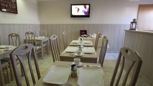 A dining area with tables set for four, chairs, a television mounted on the wall, and a small table with a lantern on the right. - Hotel Chamdor (Roeselare)
