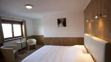 Ett hotellrum med en stor säng, ett litet skrivbord, en stol och ett fönster.