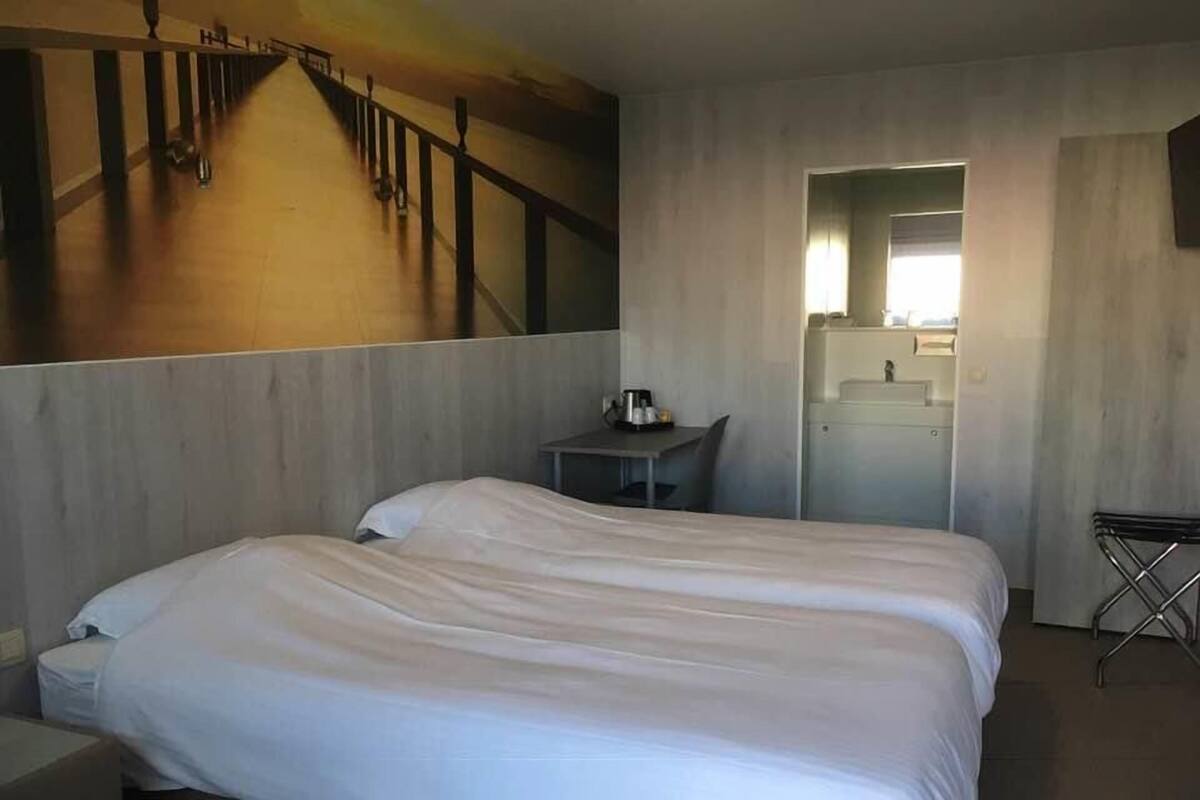 A hotel room with a large bed, a small table, a mirror, and a view of the outside.