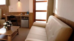 A compact hotel room with a sofa, a small dining table, a kitchenette, and a large window with curtains. - Hotel Chamdor (Roeselare)