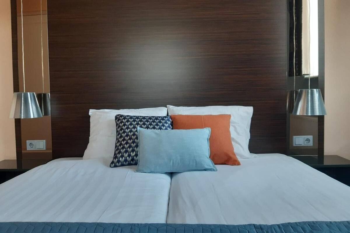 A neatly made bed with white linens, a dark wood headboard, and three pillows in different patterns and colors.