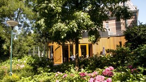 Een gebouw met een houten gevel, omringd door weelderig groen en roze bloemen.