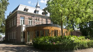 Een historisch gebouw met een bakstenen gevel, grote ramen en een moderne aanbouw met houten buitenkant.