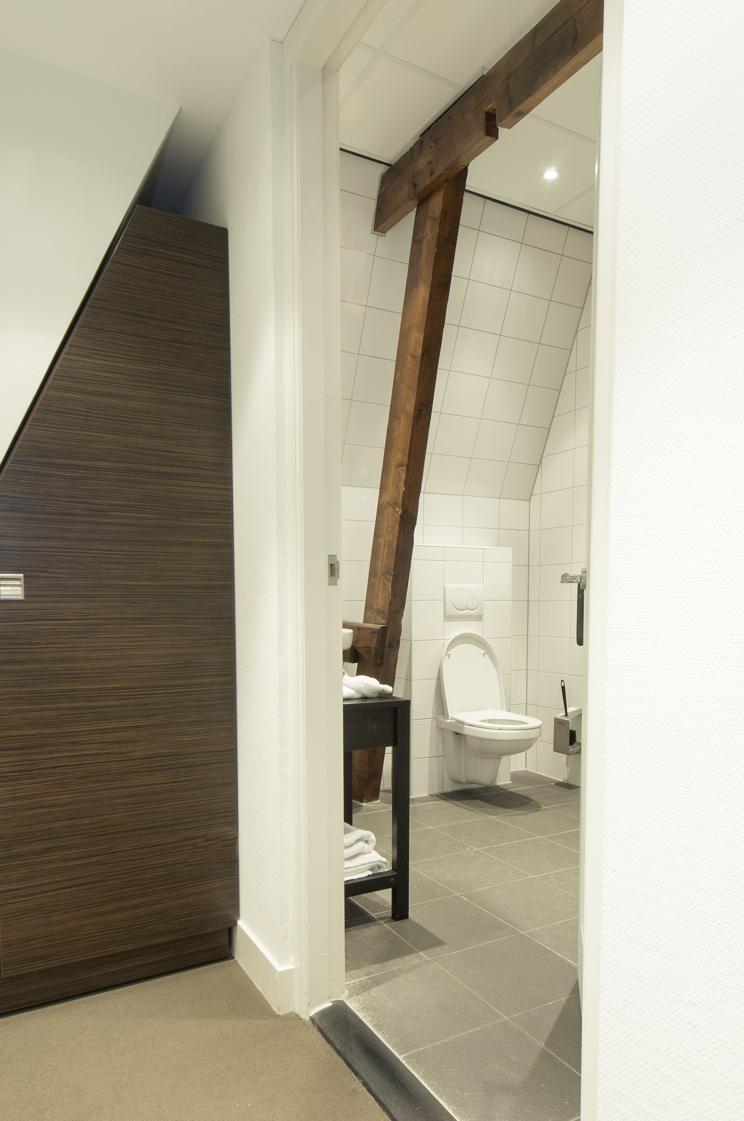 Un baño moderno con una viga de techo de madera, un inodoro blanco y piso de baldosas.