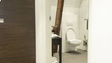 Un baño moderno con una viga de techo de madera, un inodoro blanco y piso de baldosas.
