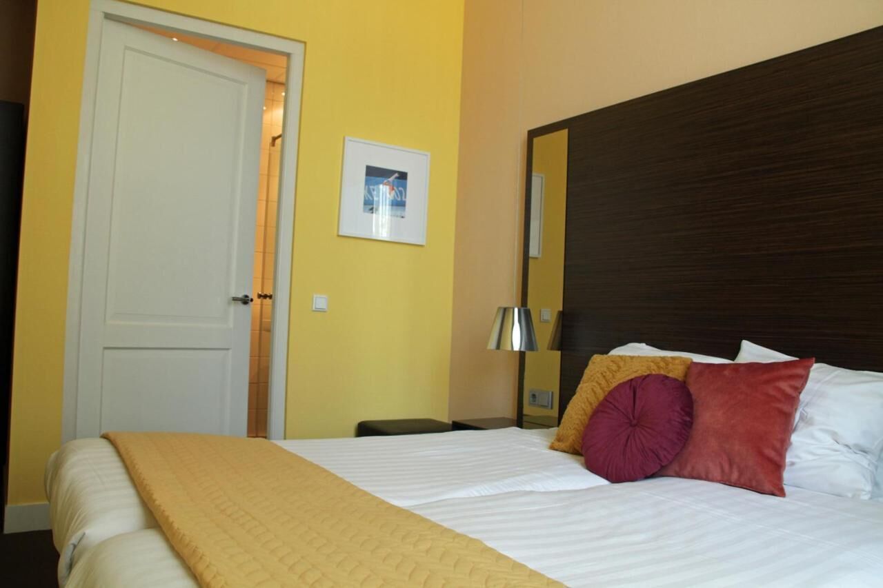 A hotel room with a bed, a bedside table, a lamp, a door, and a framed picture on the wall.