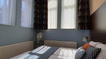 A bedroom with a bed, a chandelier, a radiator, and windows with curtains.