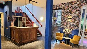 Een moderne lobby met een houten receptiebalie, een trap met rode leuningen en een accentmuur met bloemenbehang.