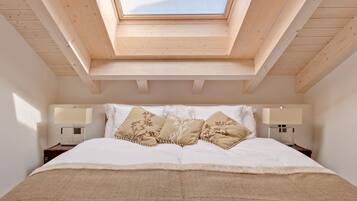 Ein Schlafzimmer mit Dachfenster, einem Bett mit weißen Leinen, zwei Nachttischen mit Lampen und einer gewebten Tagesdecke.
