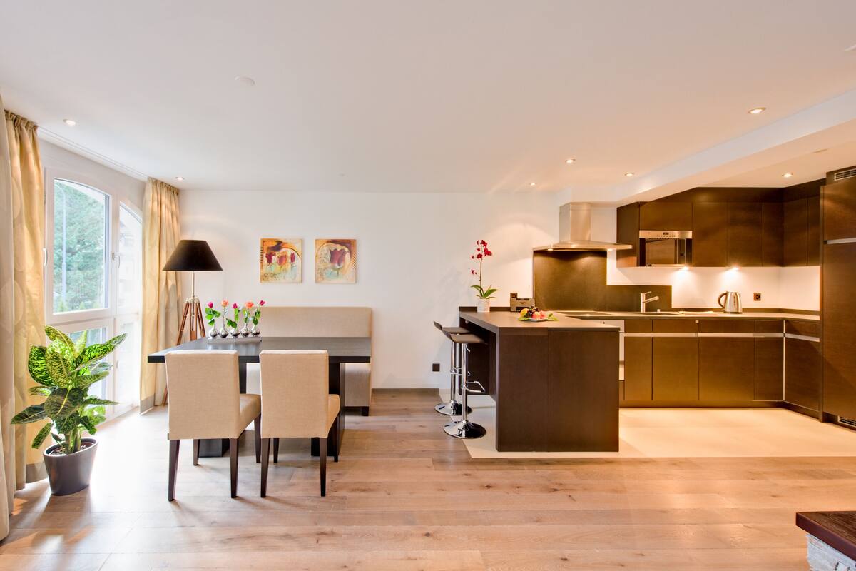 A modern kitchen with a central island, bar stools, and a dining area with a table and chairs.