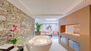 Une salle de spa moderne avec un mur en pierre, une grande baignoire et un coin salon agrémenté de coussins.