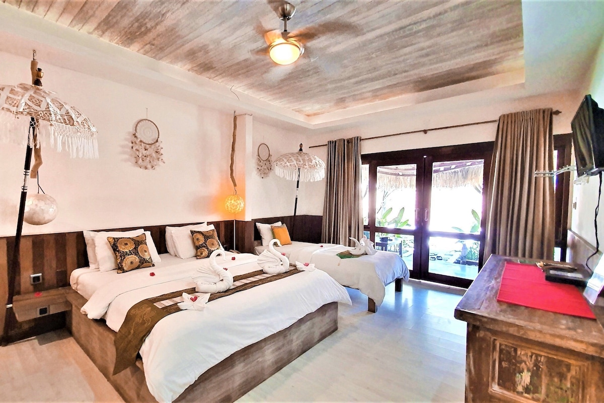 A hotel room with a large bed, two smaller beds, a desk, and a ceiling fan.