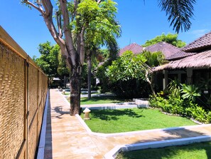 Un patio con un sendero empedrado, una valla de bambú y construcciones con techo de paja.