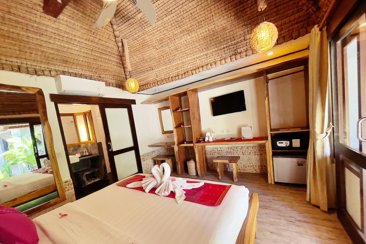 A hotel room with a bed, a small table, a TV, a mirror, and a kitchenette.