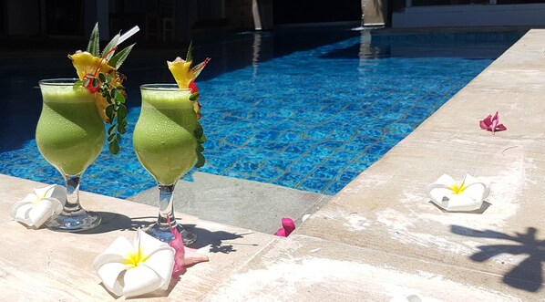 Dos cócteles verdes con adornos tropicales junto a una piscina.