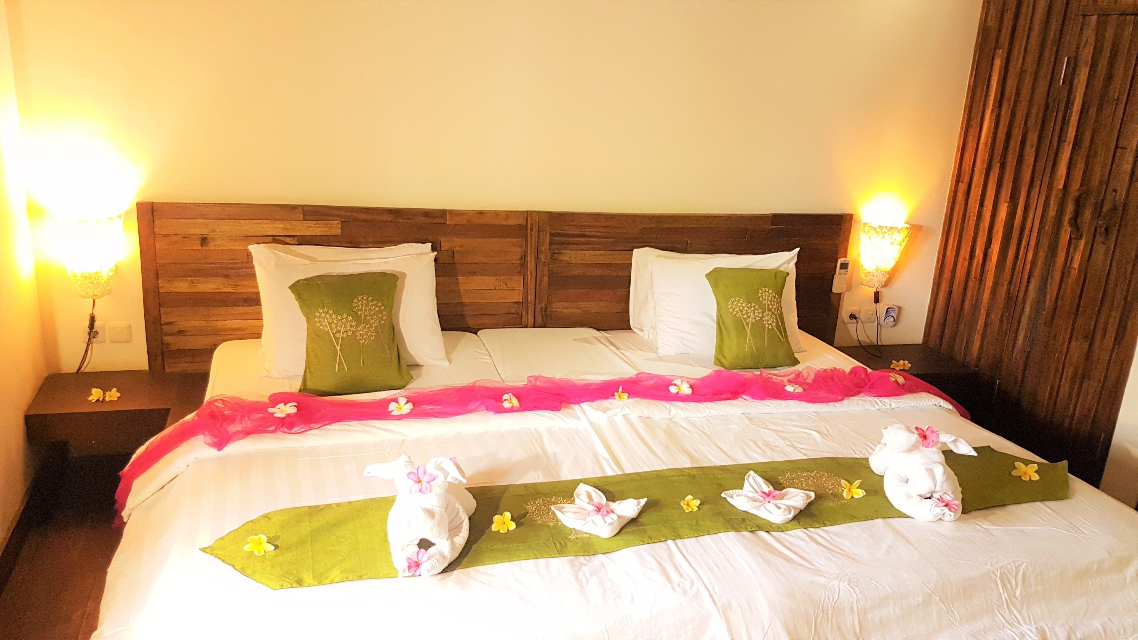 A neatly made bed with a green runner, white pillows, and decorative flowers.