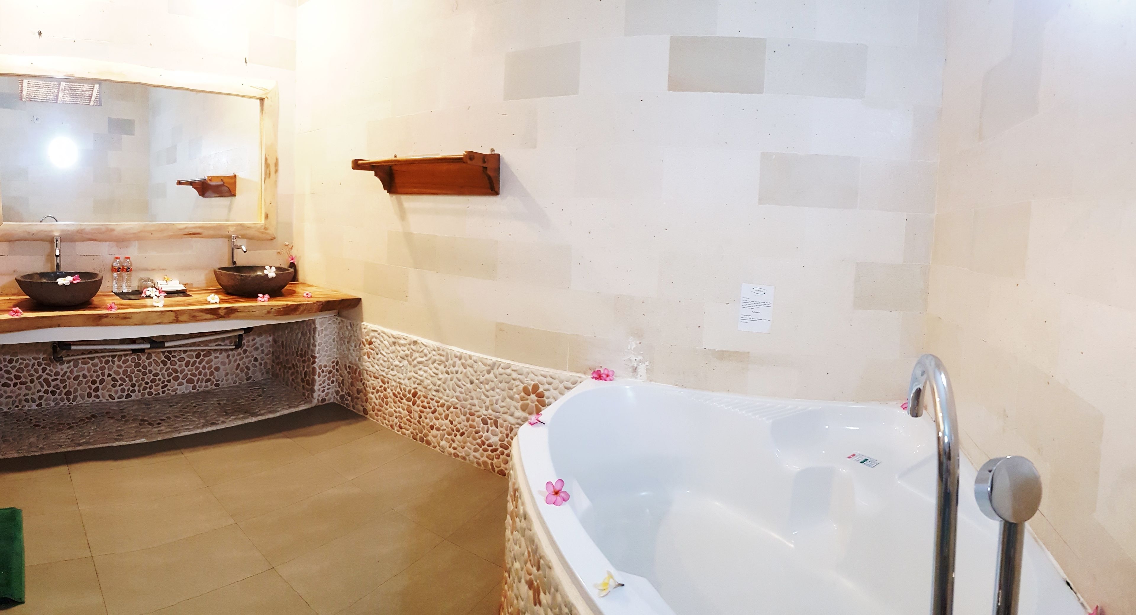 A bathroom with a stone mosaic wall, a large bathtub, and a wooden vanity with two bowls.