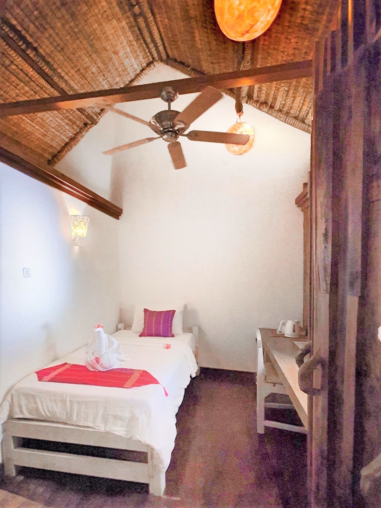 A bedroom with a bed, a bedside table, a ceiling fan, and a wall-mounted light fixture.