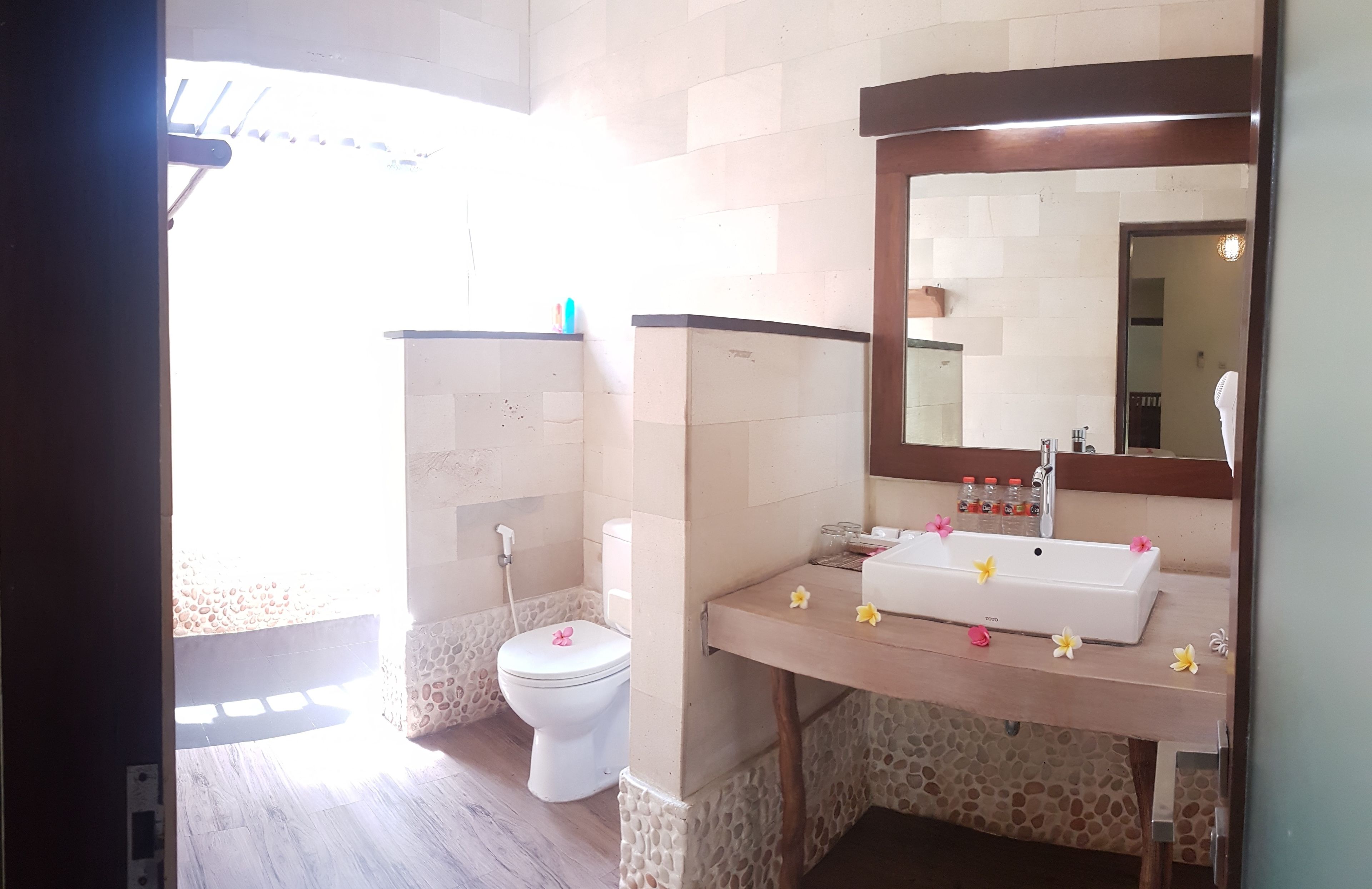 Un baño con inodoro blanco, lavamanos con espejo y zona de ducha.