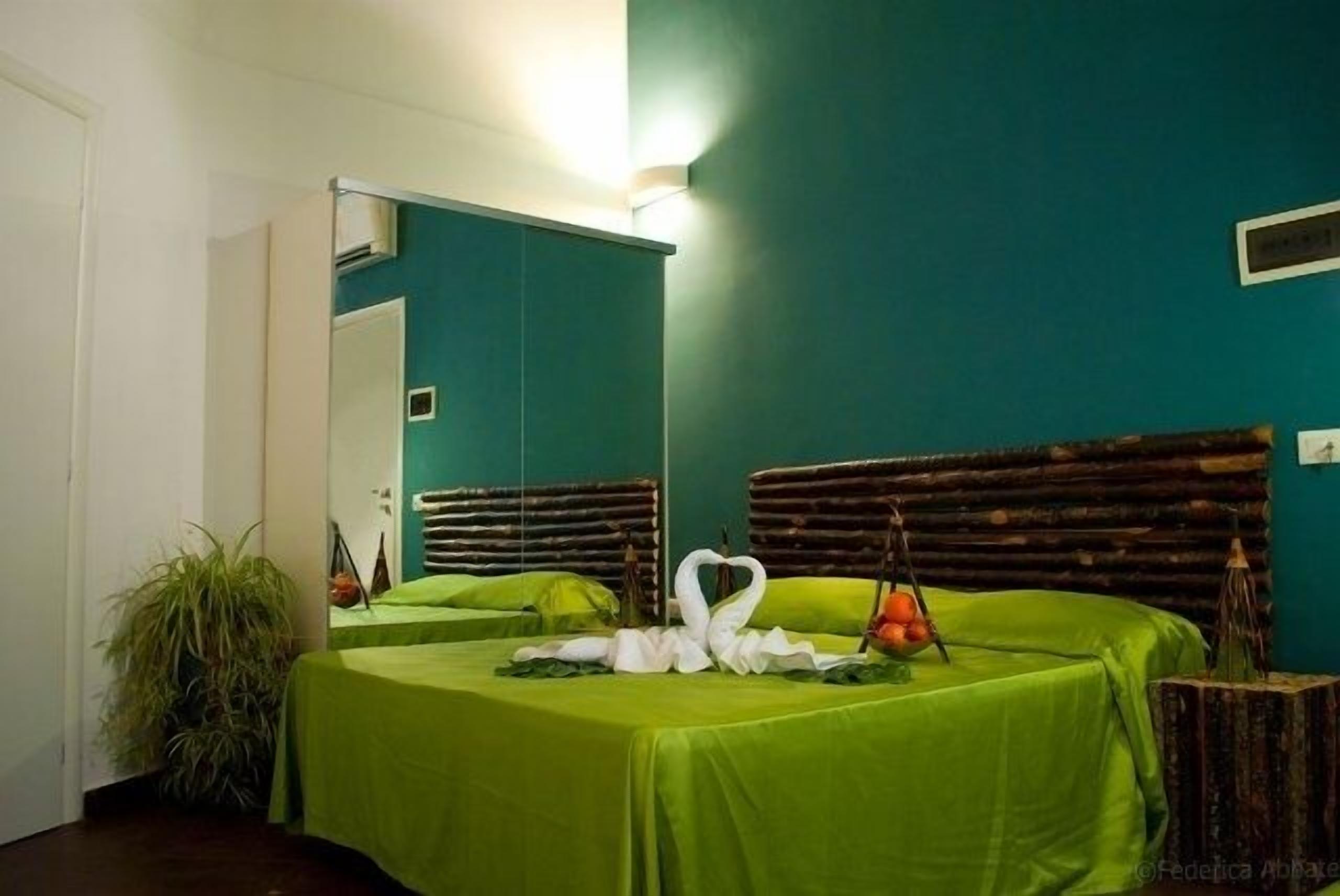 A room with teal walls, a bed with green bedding, a mirror, and a swan decoration on the bed.