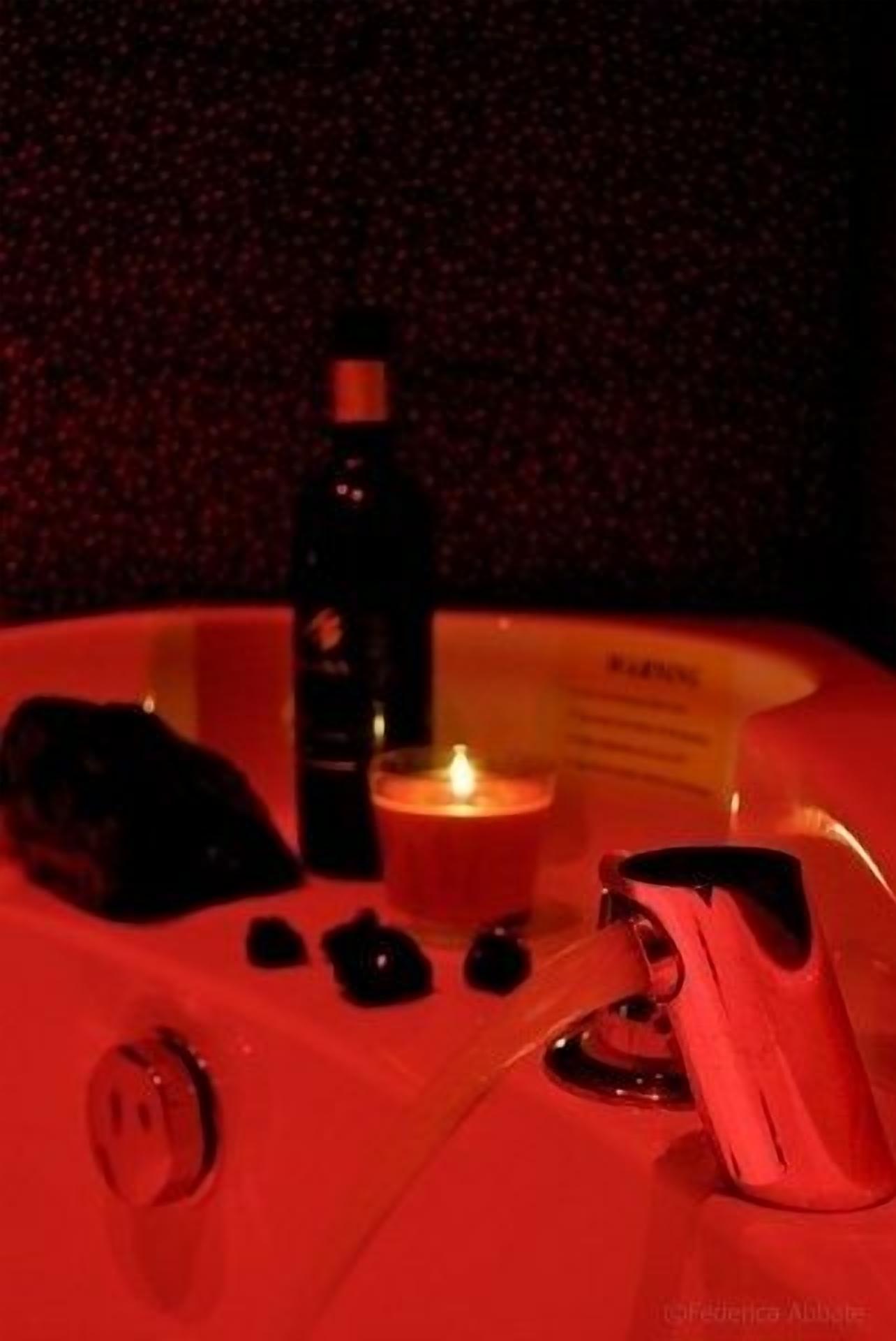 A dimly lit room with a red hue, featuring a candle, a bottle, and a small table with a few items on it.