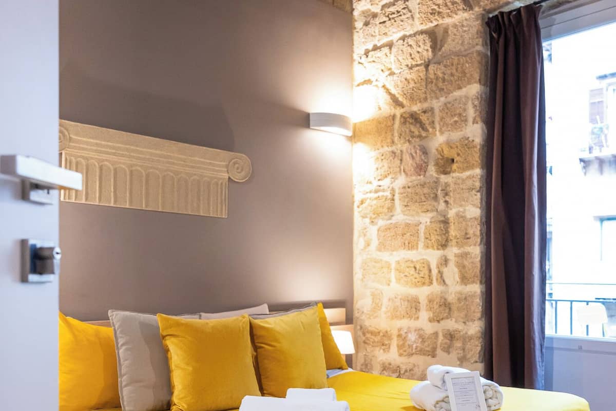 Una habitación con cama, pared de piedra y ventana con cortinas.