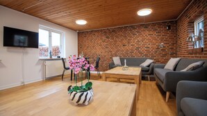 A modern living room with a brick wall, a flat-screen TV, a wooden coffee table, and two grey sofas. - Hotel Korning B&B  (Horsens)