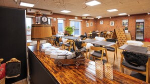 A restaurant with brick walls, wooden tables, and chairs. There are clocks on the wall, a plant, and a refrigerator. - Hotel Korning B&B  (Horsens)