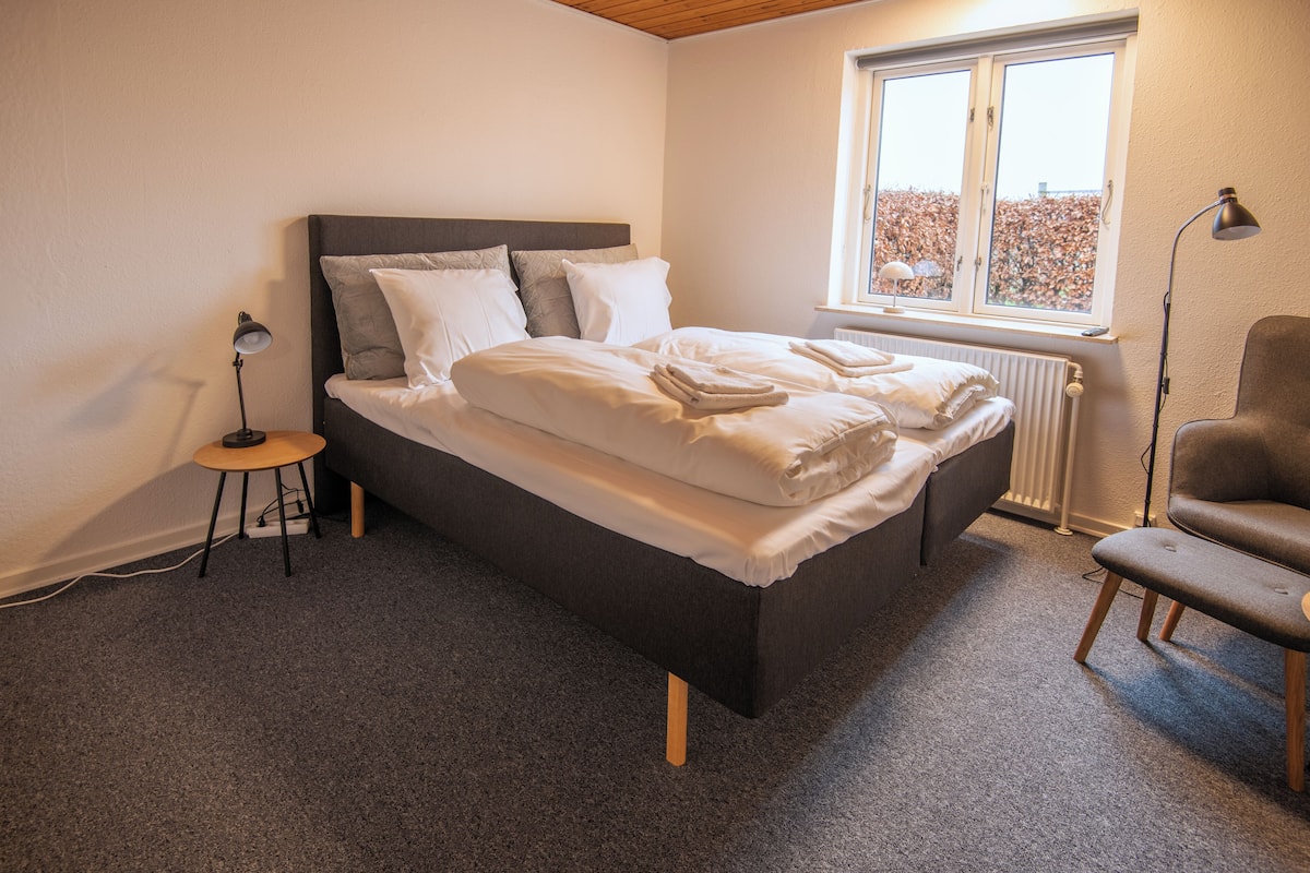 A bedroom with a bed, a chair, a lamp, and a window.