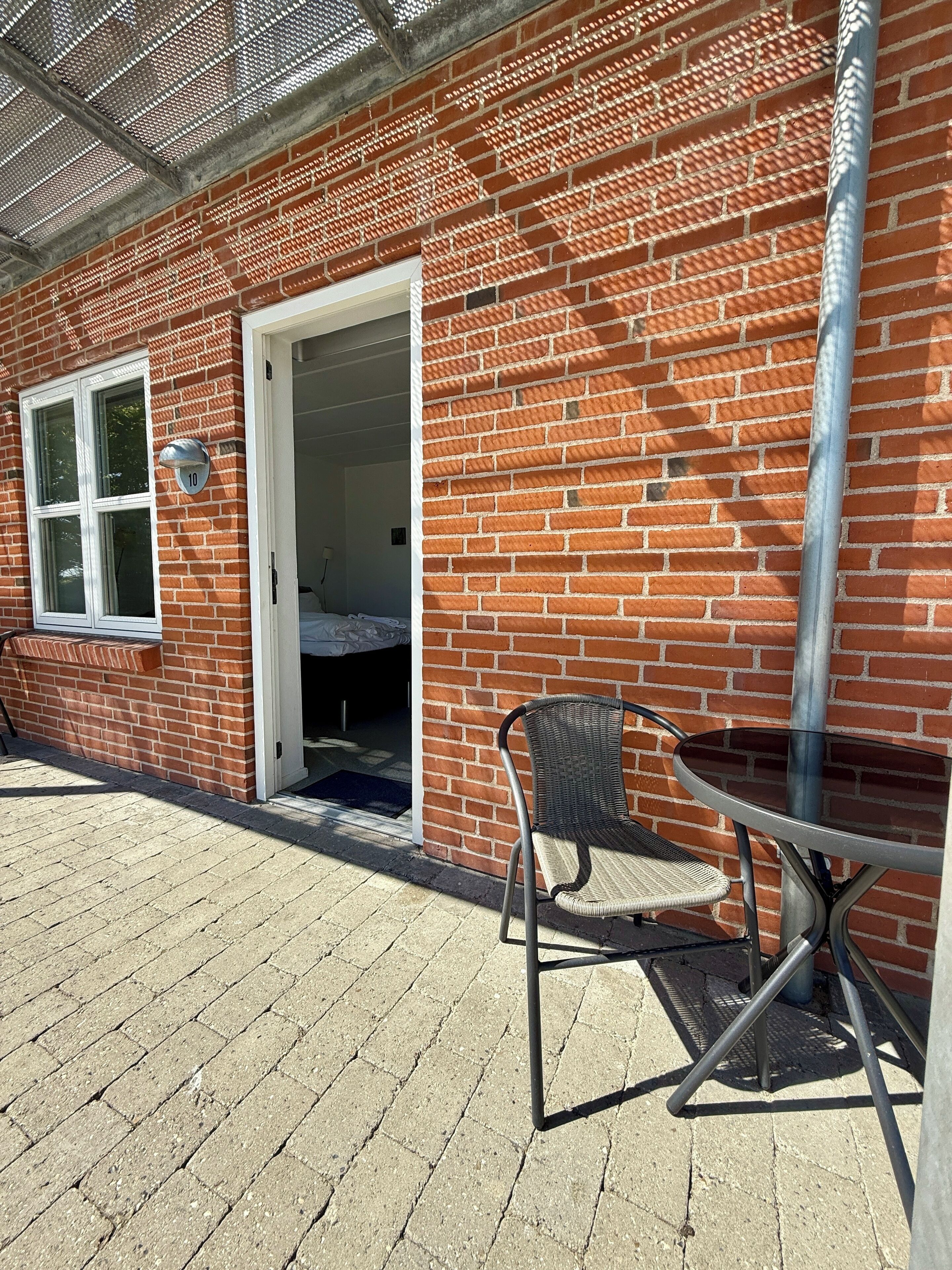 Un edificio de ladrillo con una puerta que da a una habitación, una ventana y un pequeño espacio al aire libre con una silla y una mesa.