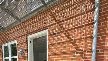 Un edificio de ladrillo con una puerta que da a una habitación, una ventana y un pequeño espacio al aire libre con una silla y una mesa.