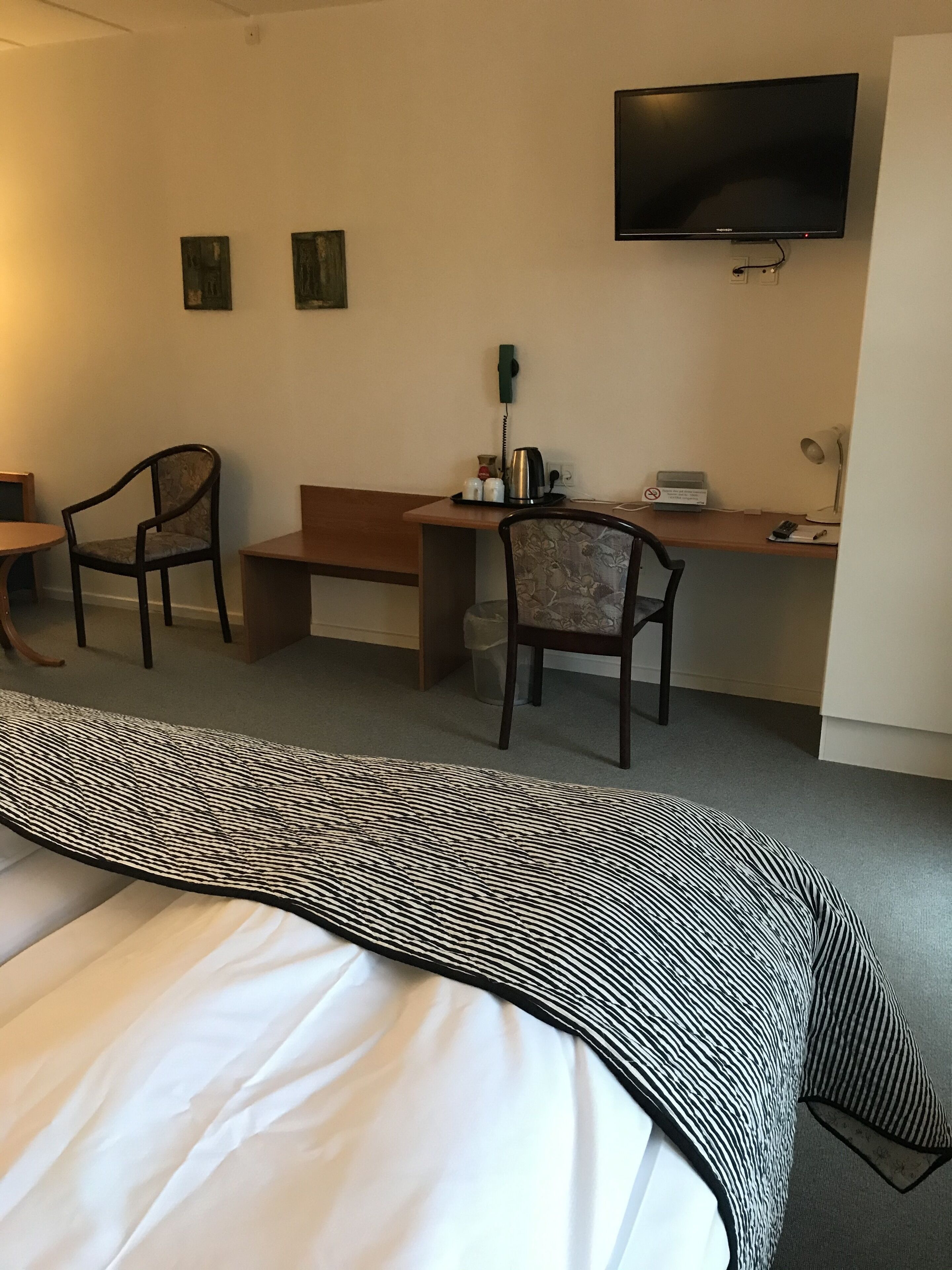 A hotel room with a bed, two chairs, a desk, a television, a telephone, and a lamp.